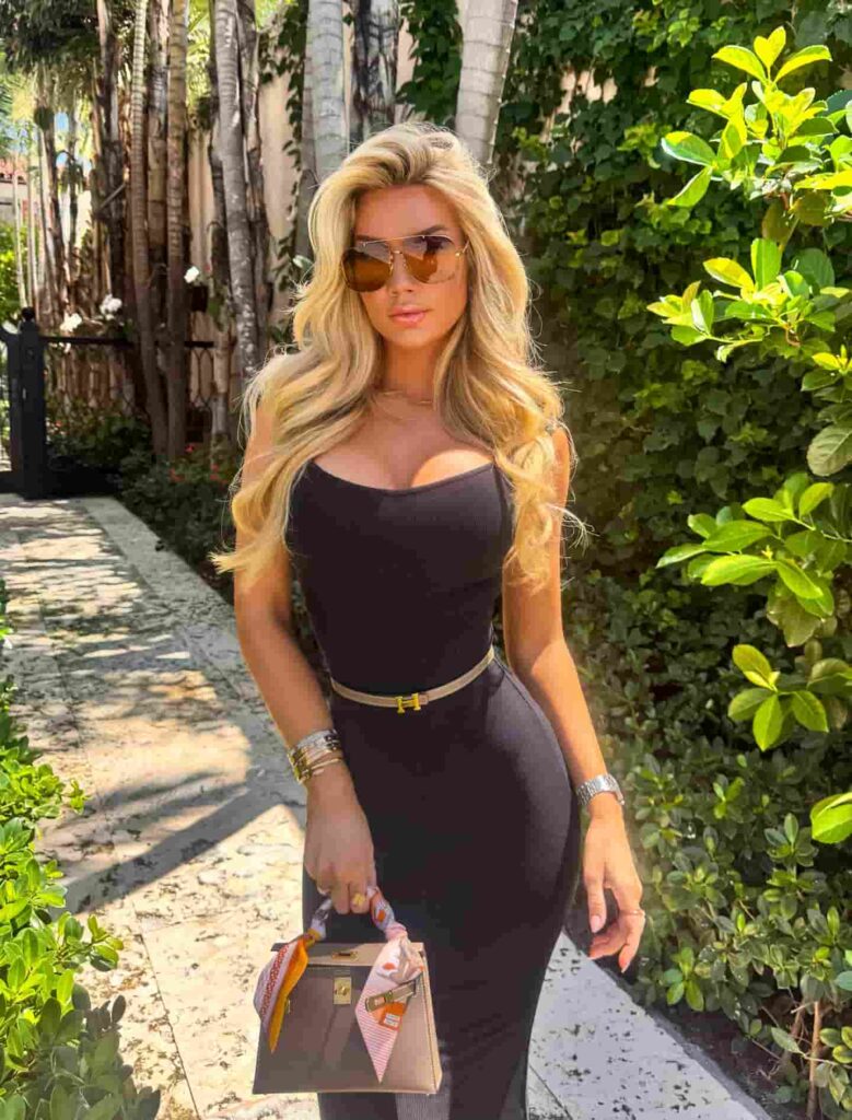 Alexa Collins showcases the ultimate luxury lifestyle aesthetic by pairing a sleek black bodycon dress with a premium designer handbag and classic aviator sunglasses for an effortlessly chic day look.